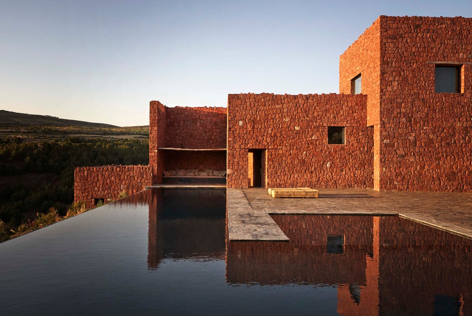 Villa E's red stone volumes reflected in the pool at dusk